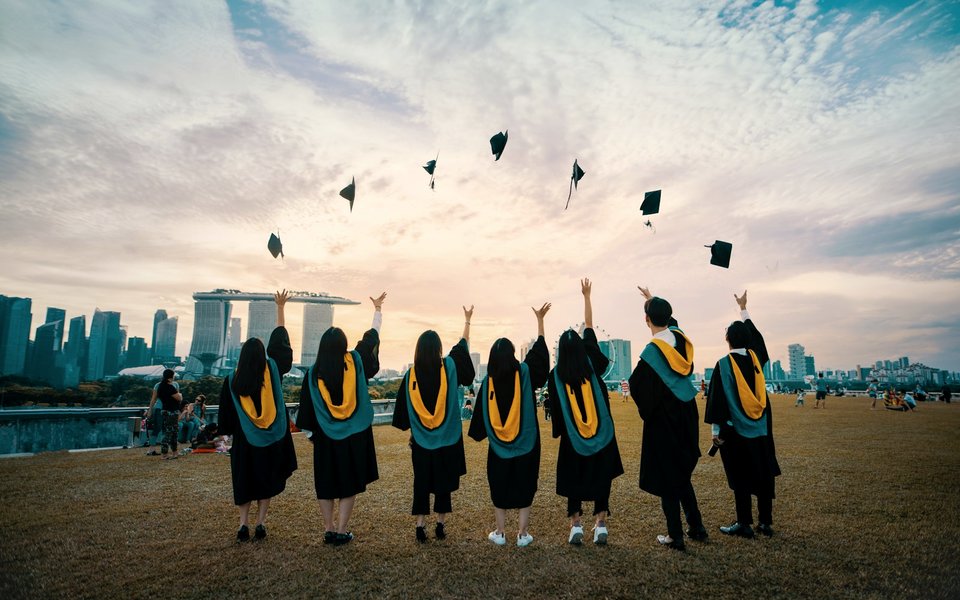 毕业生在户外抛起学位帽庆祝毕业